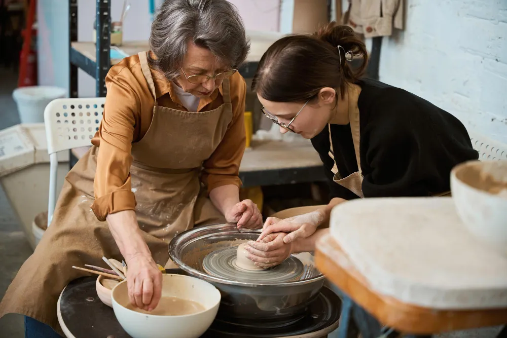 Artesana enseñando a hacer una figura de barro a una alumna en Asocación Anaisa.